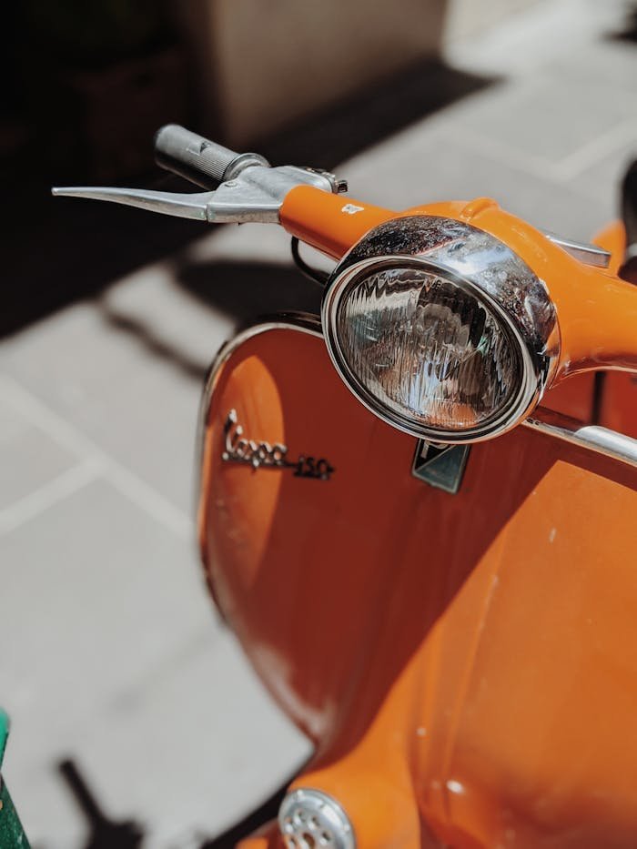 Close-up of a vintage orange Vespa scooter parked outdoors, showcasing its classic design.