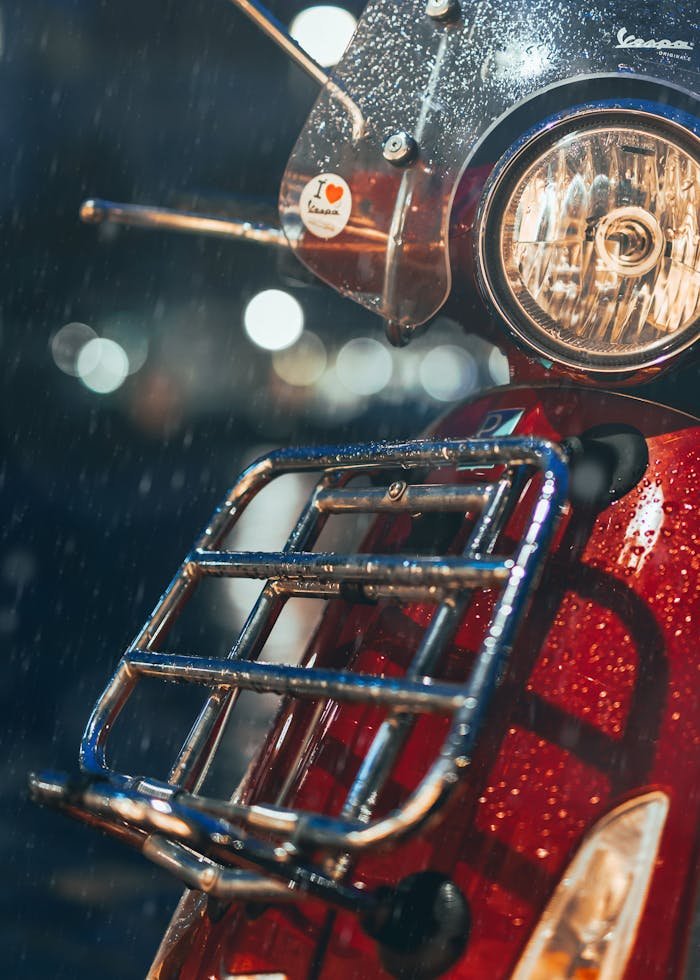 Close-up of a classic red scooter in the rain, capturing a bokeh background, evoking a vintage travel vibe.